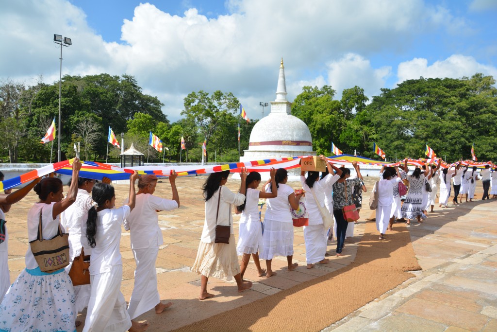 A procession of worshipers carry a long sash which they will wrap around the ancient dagoba 